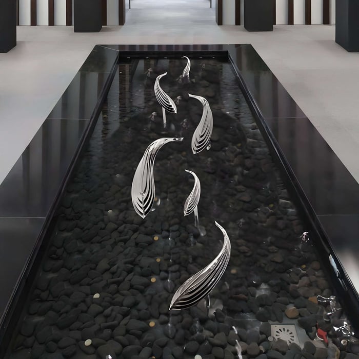 In a modern setting, Organic Fish Abstract Steel Sculptures from Giant Sculptures rise gracefully from a sleek, dark pebbled water feature.