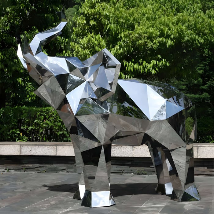 Faceted chrome elephant sculpture with geometric facets, placed on a tiled path against a backdrop of dense green foliage.