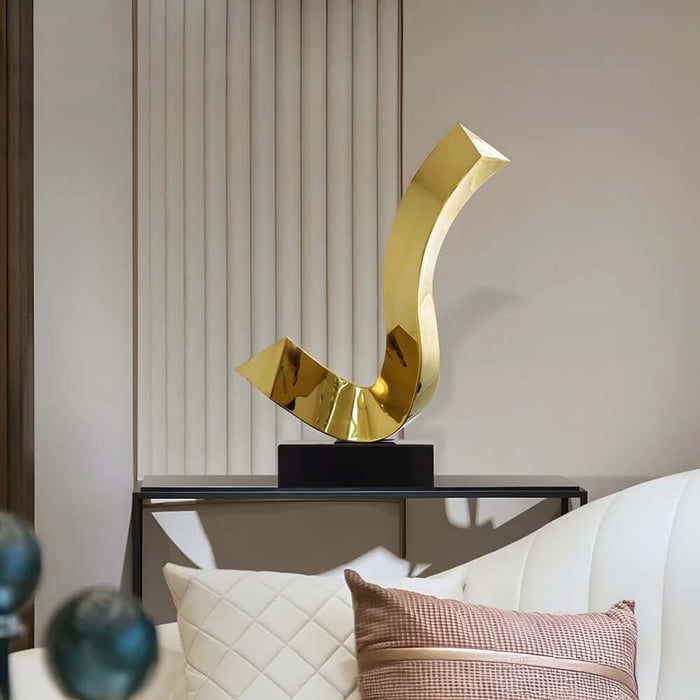 Large curved gold abstract sculpture on a console table behind a sofa, styled in a neutral modern lounge.