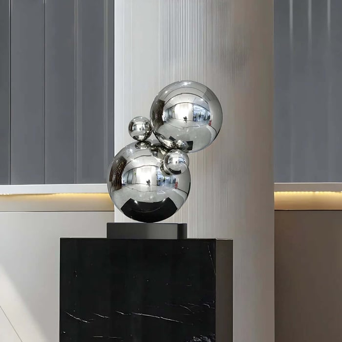 Mirror-finish stainless steel sphere geometric sculpture on a black pedestal in a minimalist space.