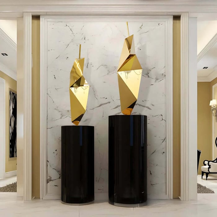 Two gold faceted geometric sculptures on black pedestals against a marble feature wall.