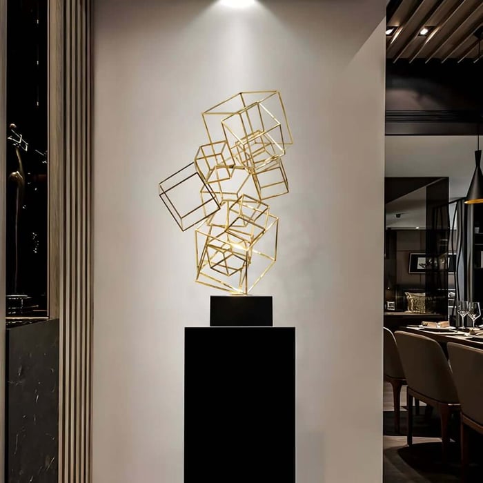 Gold wireframe cube geometric sculpture on a black plinth in a modern interior.
