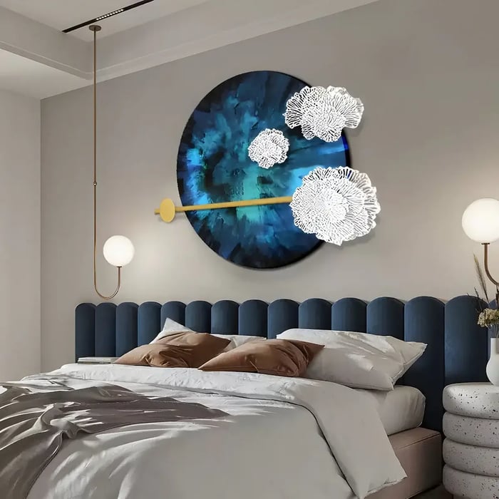 A stylish bedroom featuring a navy-blue upholstered headboard, a circular geometric art piece with white floral metal elements, and a golden accent rod extending across the artwork.