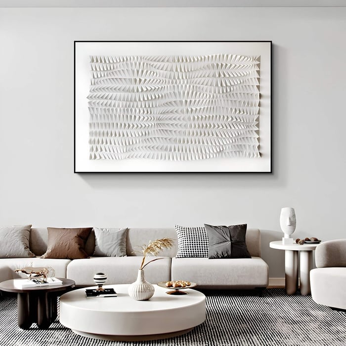 Minimalist living room with textured white geometric art in a black frame, above a soft neutral sectional sofa.