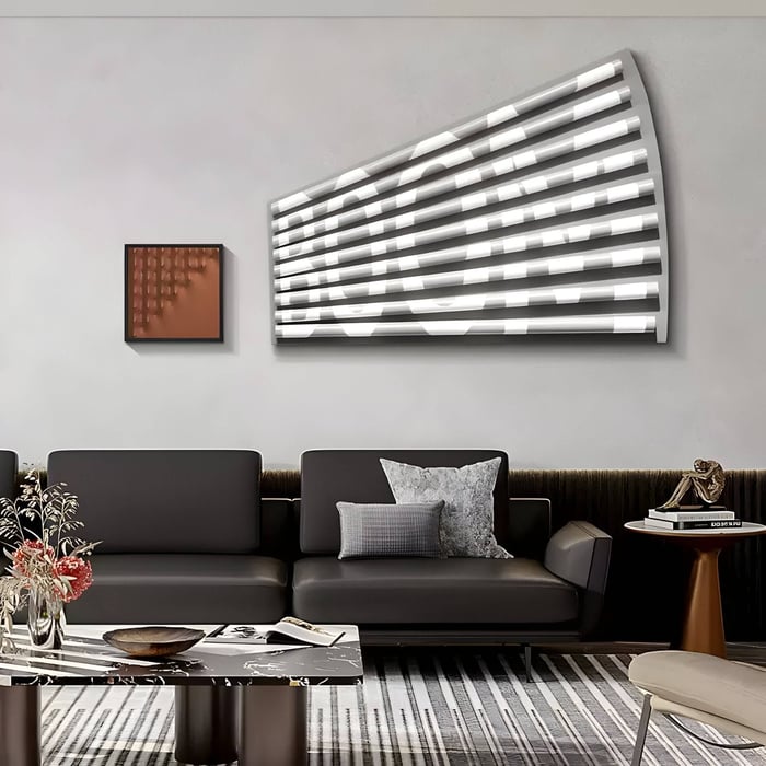 A modern living room features a gray sofa, a patterned rug, and the striking Illustra Bronze Highlight BOOM Text 3D Wooden Wall Art by Giant Sculptures with horizontal white lines on a curved surface. A small brown-tone painting sits nearby, and a side table with decor and flowers adds charm to the solid wood setting.