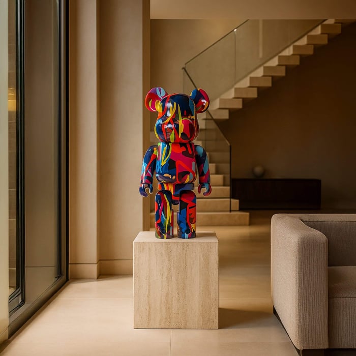 Colourful 70cm bear sculpture with bold neon graffiti-style patterns in red, blue, yellow, and green, displayed on a stone pedestal in a modern interior with neutral tones.
