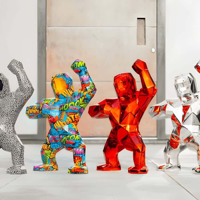  Lineup of faceted gorilla sculptures, black-and-white speckled, multicolor graffiti, translucent red, and chrome, posing with raised fists outside a modern door.