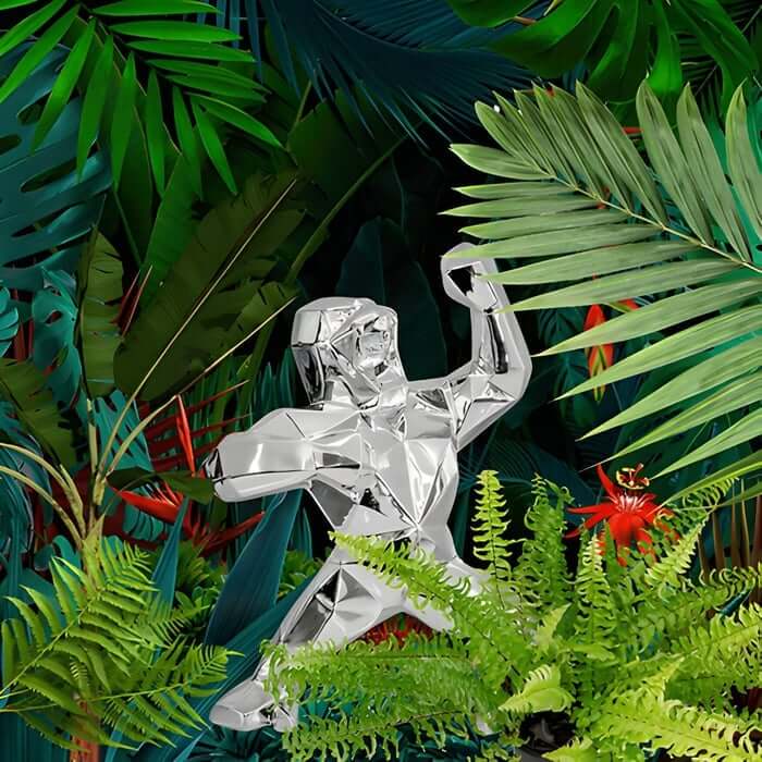 Silver low poly gorilla sculpture posing among lush tropical jungle plants.