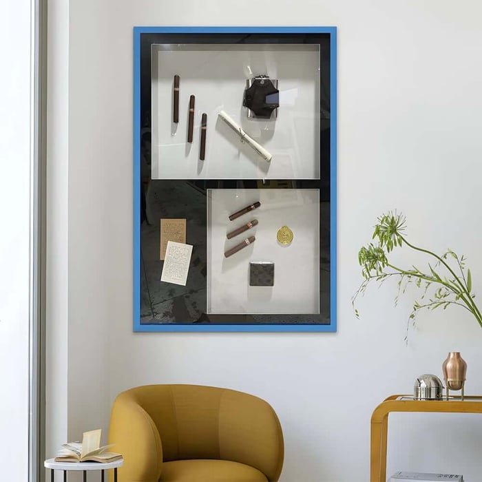 Framed contemporary hallway art display with sculptural objects in blue frame above mustard chair.