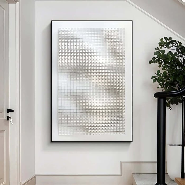 White geometric hallway artwork with raised square grid hanging near a staircase and indoor plant.