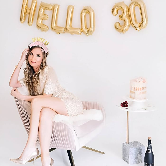 a woman sitting in a cream chair with a cake and 30 years balloons