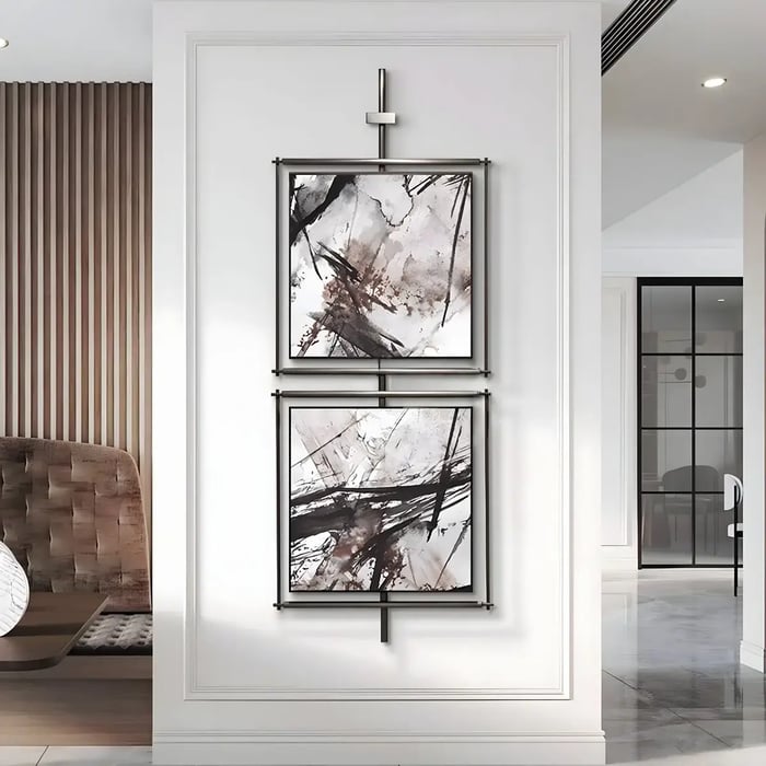 A stylish interior featuring two vertically arranged square-framed abstract paintings with black and white brushstroke designs, mounted on a sleek black metal structure.