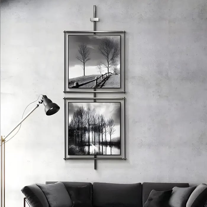 A minimalist living space featuring two vertically arranged framed black-and-white landscape photographs with a metallic hanging system.