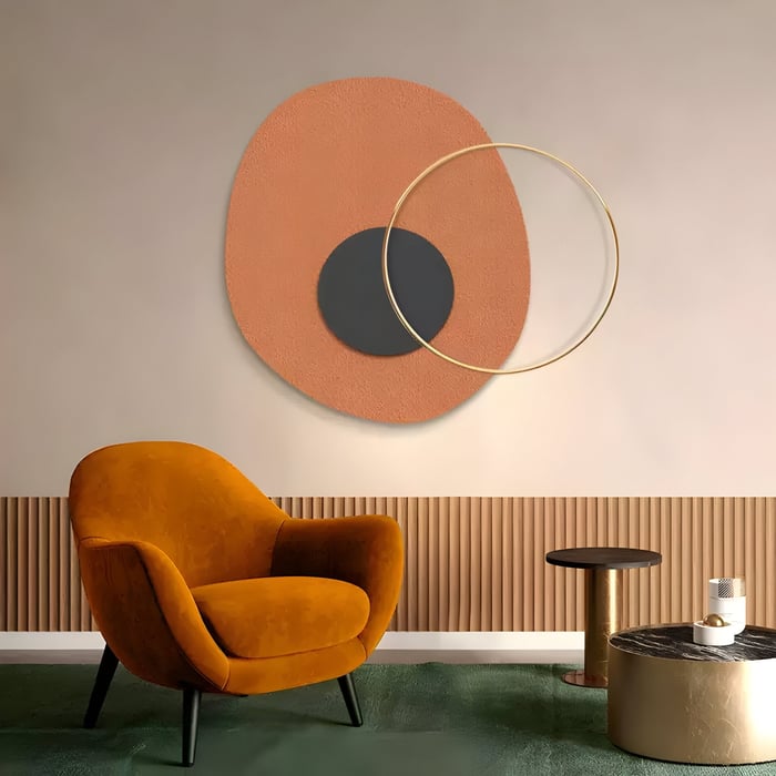 Orange & Black Circle Abstract Wall – Minimalist wall sculpture with burnt orange & black concentric shapes and gold ring above mustard chair.