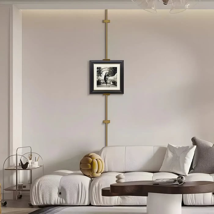 Minimalist black-and-white framed artwork on a unique rail system – A small framed print suspended by a vertical rail above a white sofa.