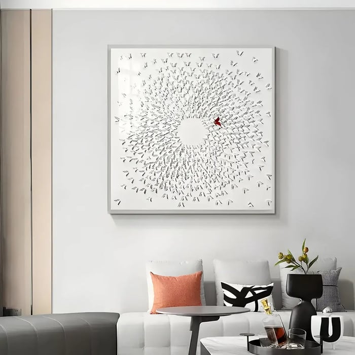 A minimalist living space with a textured white wall art piece displaying a swirling pattern of small 3D birds, accented by a single red figure.