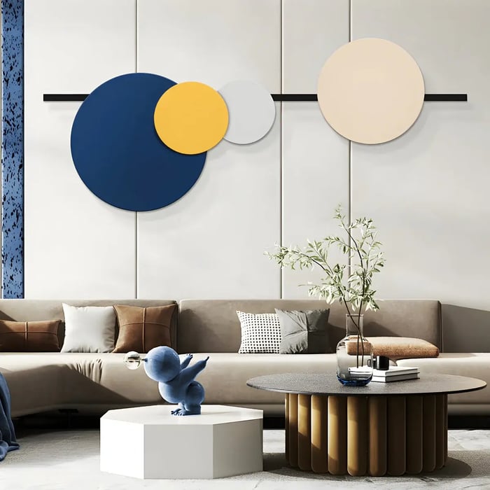 A modern living area with an abstract arrangement of large, overlapping circular panels in blue, yellow, and beige, mounted above a neutral-toned sofa.