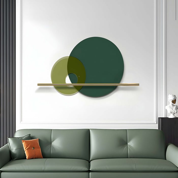 Minimalist Green and Gold Circular Wall Art – A modern wall sculpture featuring two overlapping green-tinted glass circles balanced on a sleek gold metal bar, installed on a white paneled wall above a green sofa in an elegant living room.