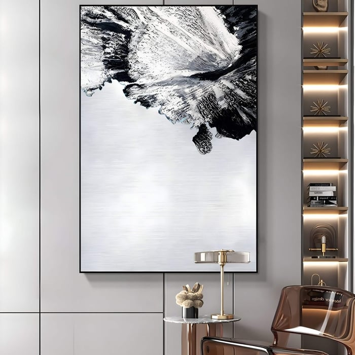 A modern living room displays the Terranica Monochrome Flow Textured Abstract Metal Wall Art by Giant Sculptures. Its black and white textures complement a small table with decor below, while shelves to the right hold books. A partially visible brown chair adds warmth to the stylish space.