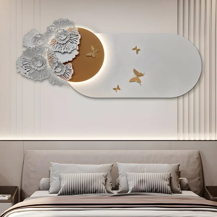 Elegant bedroom with abstract wall art above the bed – A modern bedroom featuring a neutral-toned bed with striped pillows and an oversized abstract wall sculpture. The artwork combines a curved mirror, metallic floral elements, and golden butterflies, with a glowing crescent accent adding a soft ambient effect.