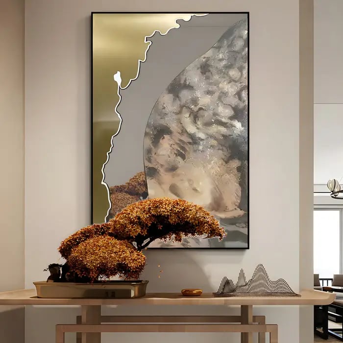 A modern interior with an abstract metallic and glass wall art featuring fluid textures and reflective surfaces. Below it, a decorative wooden console holds a sculpted bonsai tree with golden foliage and a minimalist landscape sculpture, adding a serene and artistic touch.