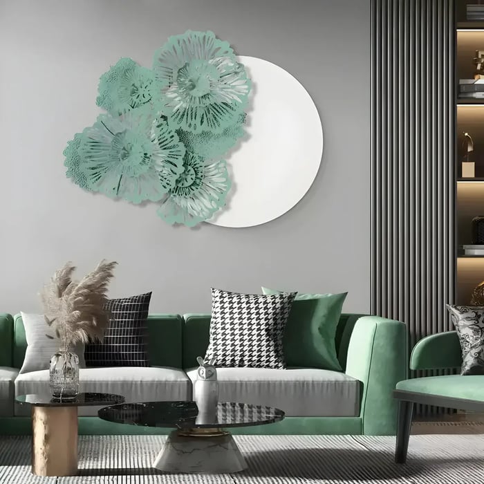 A contemporary living room with a green velvet sofa, a monochrome accent pillow, and a large decorative floral metal wall sculpture in teal and white mounted on a round mirror.