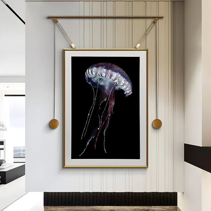 A dramatic framed jellyfish artwork with glowing details on a black background, elegantly displayed with a gold hanging mechanism in a modern hallway.