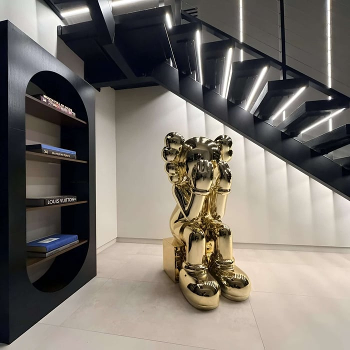 Gold metallic Iconify melancholy sitting sculpture under a staircase in a luxury minimalist interior.
