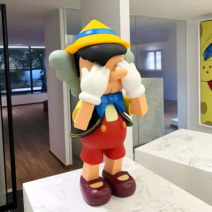 Colourful Pinocchio-inspired Iconify sculpture covering its eyes on a white marble plinth in a bright office.