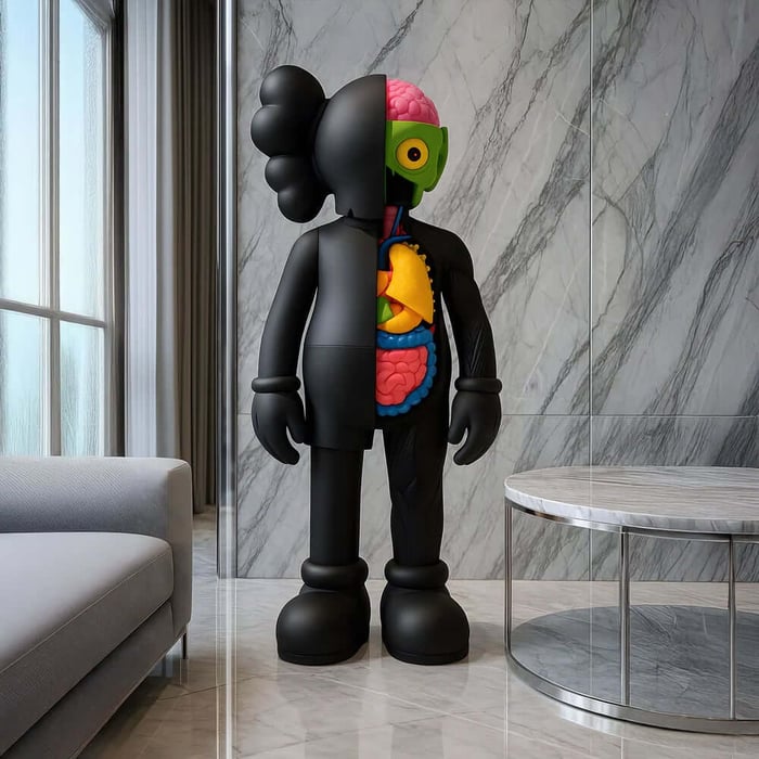 Large black half-dissected Iconify anatomy sculpture in front of a marble wall beside a modern grey sofa.
