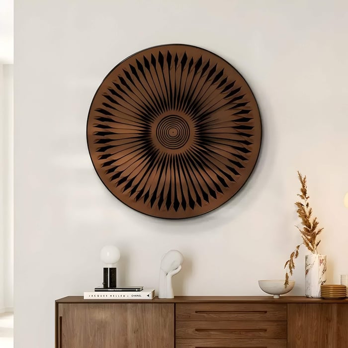 Round brown 3D wall art with radial folded leather detailing and black geometric cutouts, mounted above a wooden sideboard in a contemporary interior with minimalist decor.