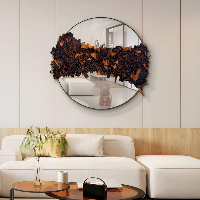 Round wall mirror with sculptural amber and black leather folds across the centre, mounted in a modern living room above a cream sofa and amber-toned coffee table.