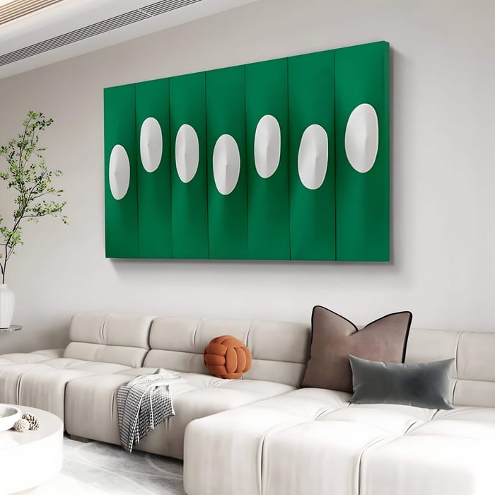 Bold green and white 3D wall art with oval sculptural discs arranged in a rhythmic sequence, mounted above a cream tufted sectional sofa in a minimalist living room.