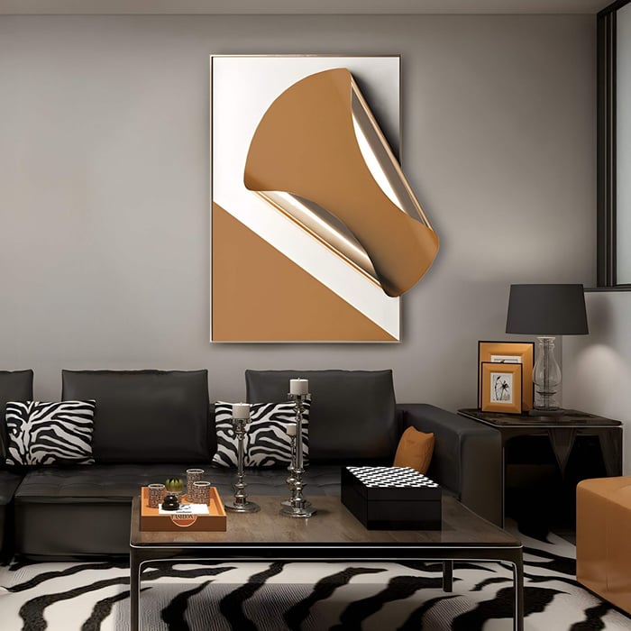 Vertical 3D wall art with a folded sculptural metal form in amber and white tones, mounted above a black leather sofa in a bold living room with zebra-print cushions and decor accents.