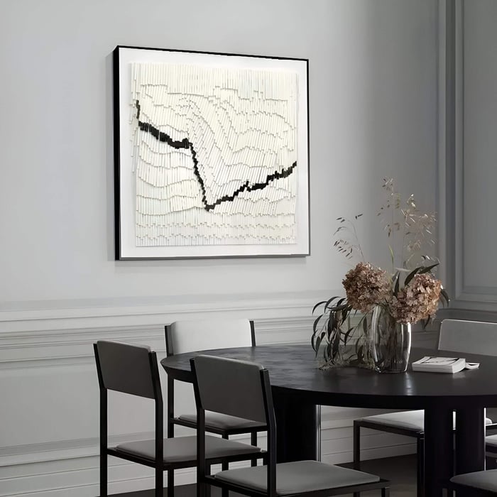 Framed 3D wall art featuring layered white paper strips with a jagged black vein-like line running through, displayed above a black round dining table in a minimalist grey-toned room.