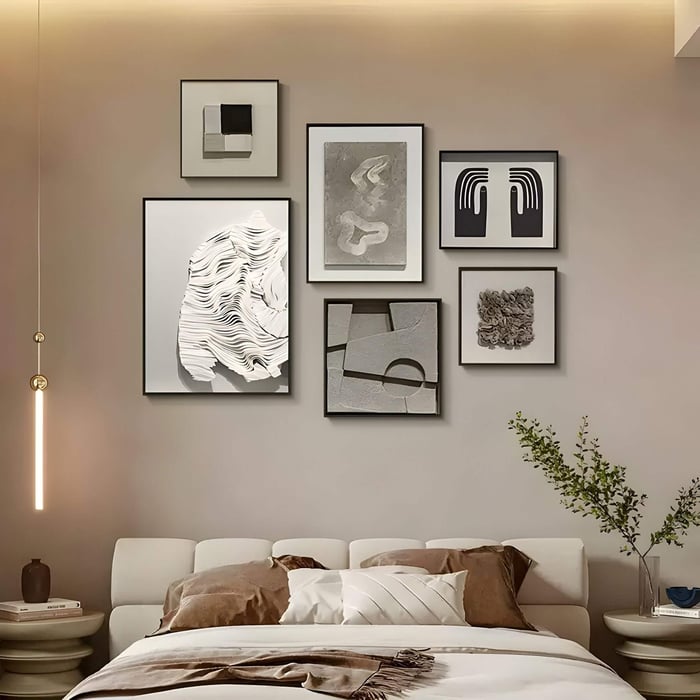 Gallery wall of six framed 3D neutral artworks featuring layered textures, abstract shapes, and sculptural reliefs, styled above a contemporary bed with earth-toned bedding and soft ambient lighting.