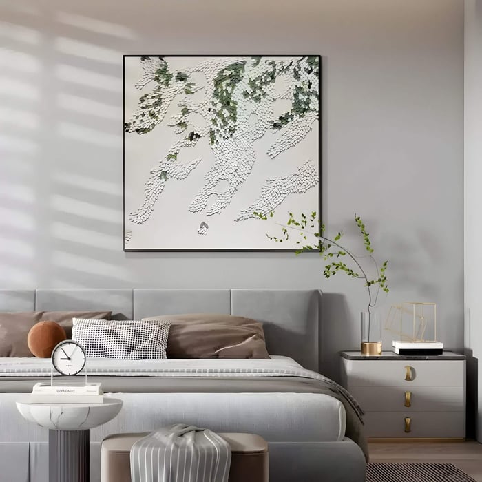 Square 3D wall art featuring layered white and green leather scale-like textures in an abstract drifting pattern, mounted above a grey bed in a softly lit modern bedroom.