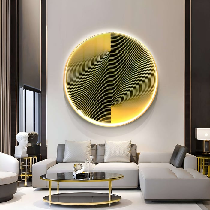In a modern living room, the Astral Gold Crystal Porcelain LED Wall Art from Giant Sculptures showcases a large circular abstract piece. A gray sectional sofa complements a black glass coffee table with an aluminum frame, creating neutral decor and warm ambiance.