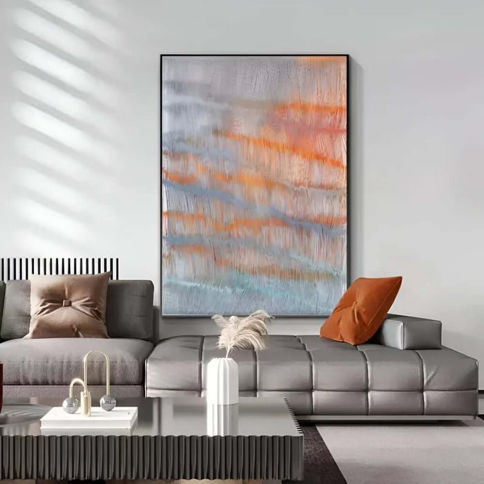 Large living room art abstract orange and grey painting hanging above a modern grey sectional sofa in a minimalist living room.