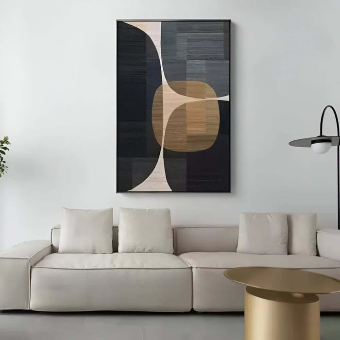 Tall abstract geometric painting in dark navy, beige and tan tones hanging above a cream sofa and gold coffee table.