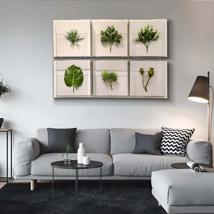 Set of six framed botanical prints with green leaves displayed over a grey sofa and black rug in a contemporary living room.