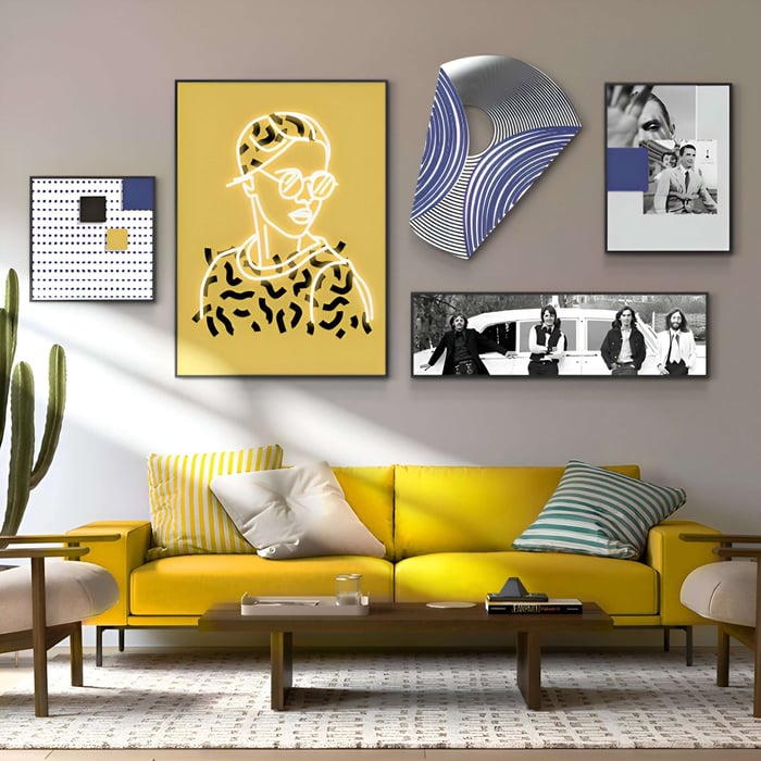 A modern living room has a bright yellow sofa with striped cushions. Art pieces, including a Giant Sculptures Orison Geometric Play Crystal Porcelain 3D Wall Art, a neon portrait, and black-and-white photos decorate the space. A cactus stands beside a wooden coffee table in front.