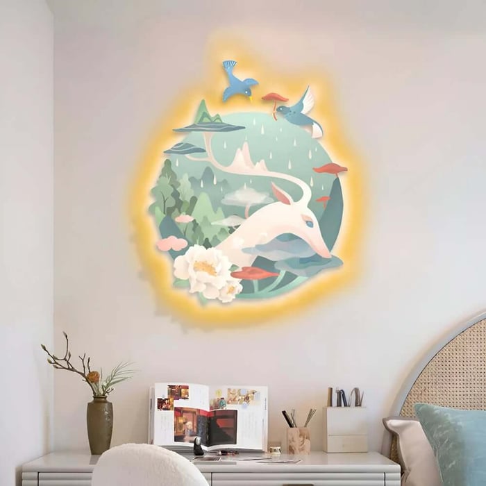 Playful wall mural above a desk showing a white deer in a dreamy landscape with mountains, trees, flowers, and flying birds, surrounded by a soft halo glow.