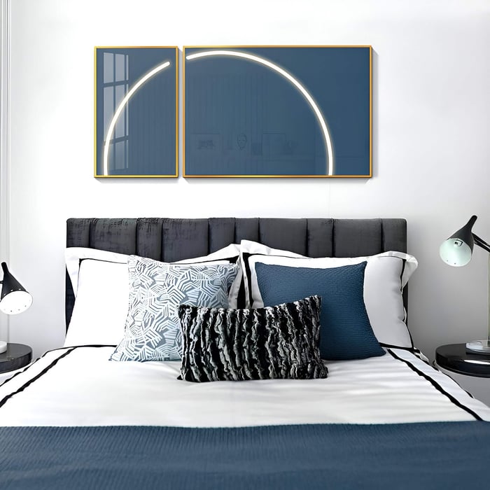 Contemporary bedroom with dual-panel blue wall art featuring a glowing arc, above a stylish bed with monochrome pillows.