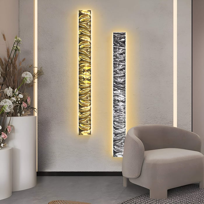Artistic illuminated textured wall panels in gold and silver tones, beside a cozy neutral armchair.