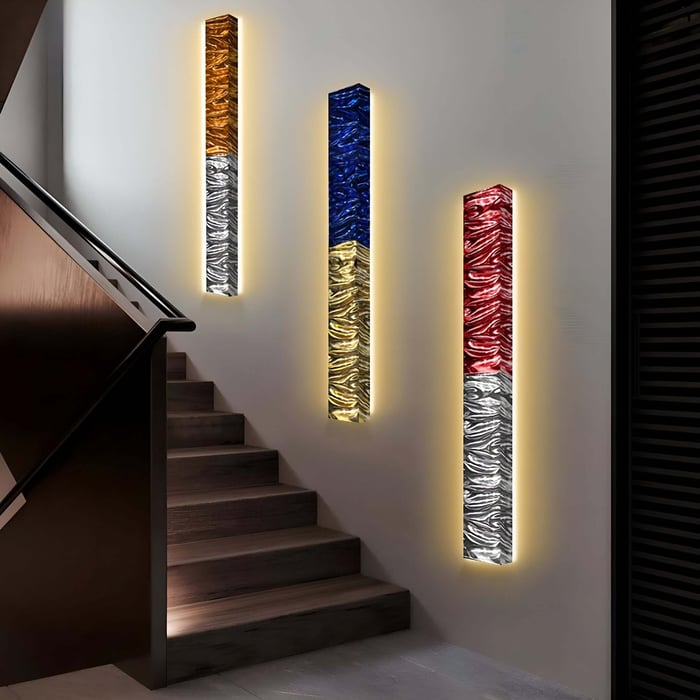 Three Textura 3D wall lights from Giant Sculptures illuminate the stairs. Each is a piece of art, featuring copper and silver, blue and yellow, along with red and silver leather designs. These cast a warm glow, creating an inviting ambiance reminiscent of sophisticated wall art.
