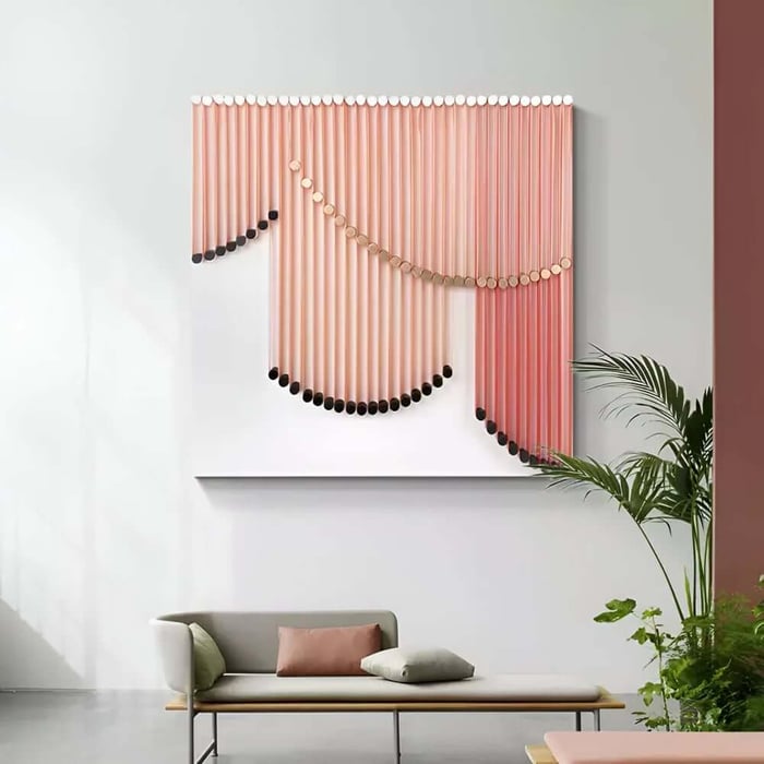 Modern living room with a minimalist bench, soft pastel cushions, indoor plants, and a large pink and gold 3D wall art piece featuring cascading rod-like elements.