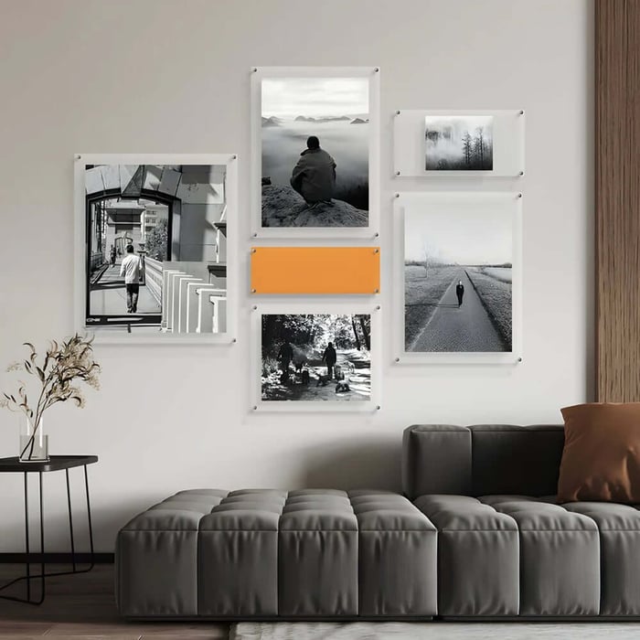Minimalist gallery wall of black-and-white photos in clear frames above a grey sectional sofa.