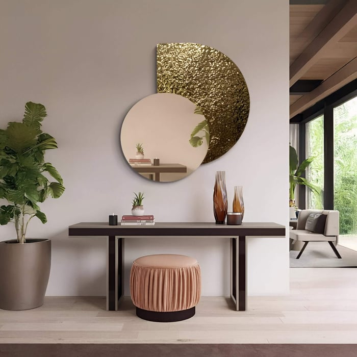 A modern hallway featuring a round mirror art piece with overlapping gold and reflective circular panels above a sleek console table, styled with vases and a velvet stool for a refined contemporary look.
