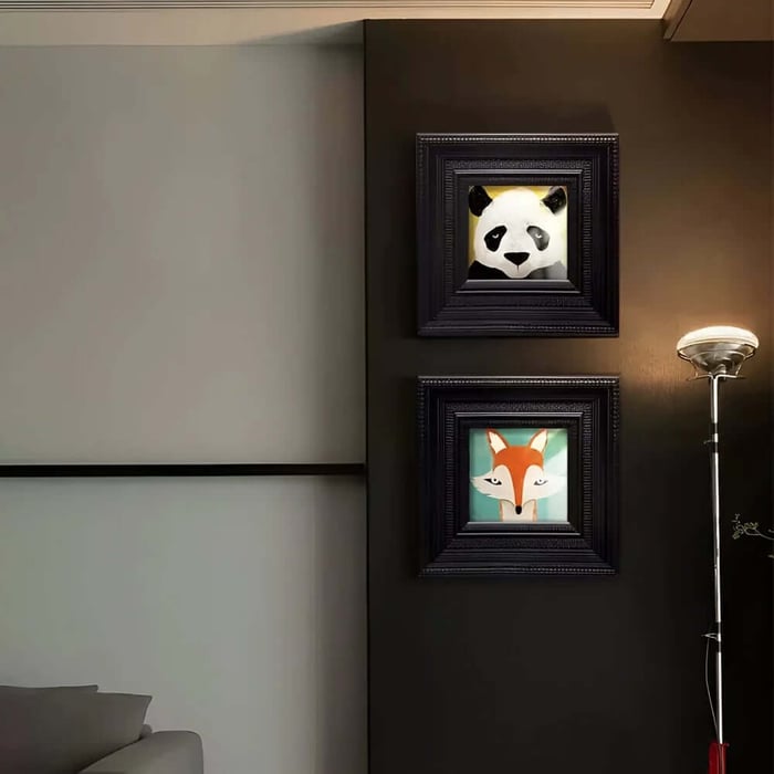 Dark, moody corner wall holding two stacked black frames a panda portrait above and a fox portrait below next to a chrome floor lamp.